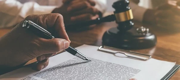 mężczyzna podpisujący dokument na biurku prawnika