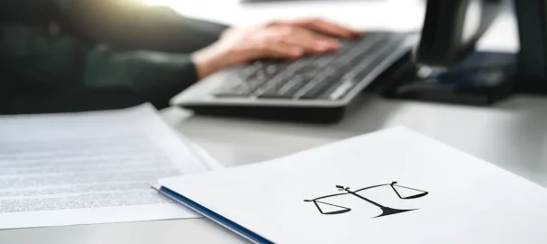 osoba pisząca na laptopie oraz folder z symbolem wagi
